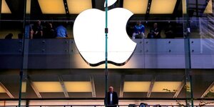 Un client se tient sous un logo apple illumine alors qu'il regarde par la fenetre du magasin apple situe dans le centre de sydney
